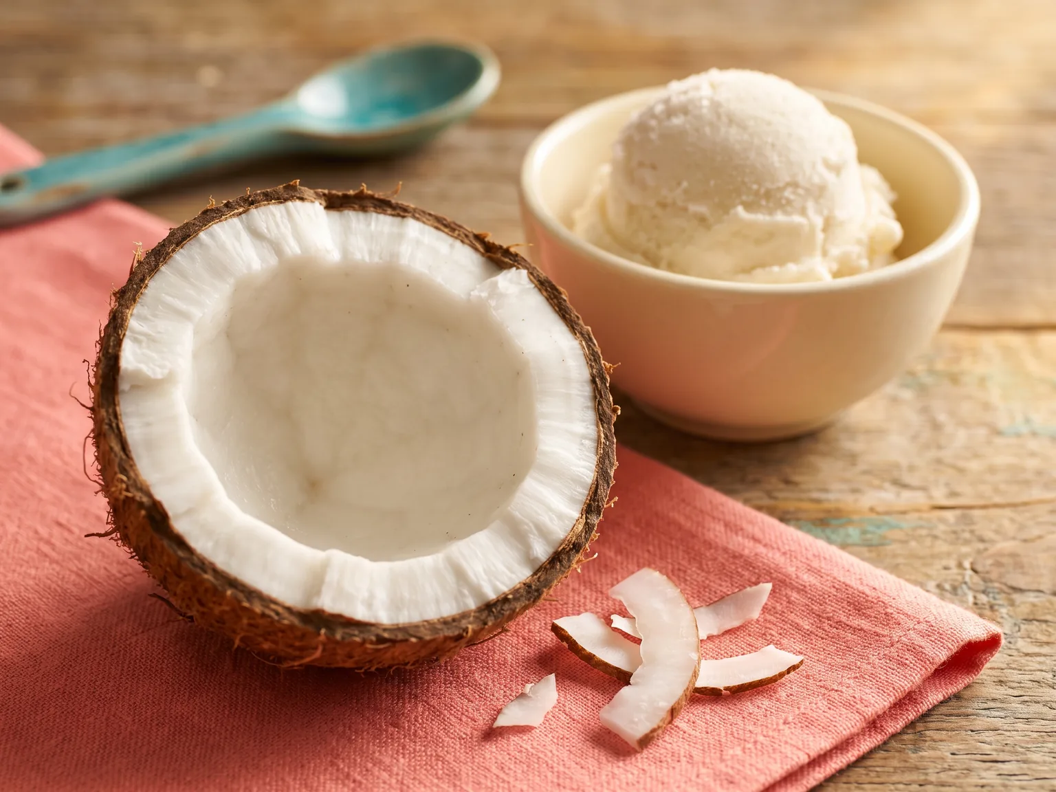 A cut coconut and shavings on a coral napkin with a pale scoop behind